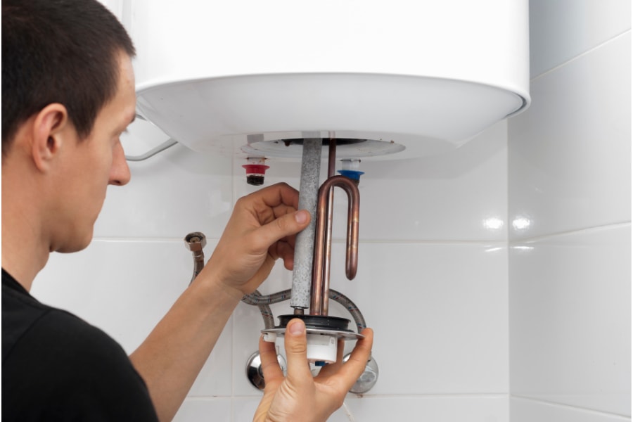 Plumber fixing immersion heater within wall mounted hot water system